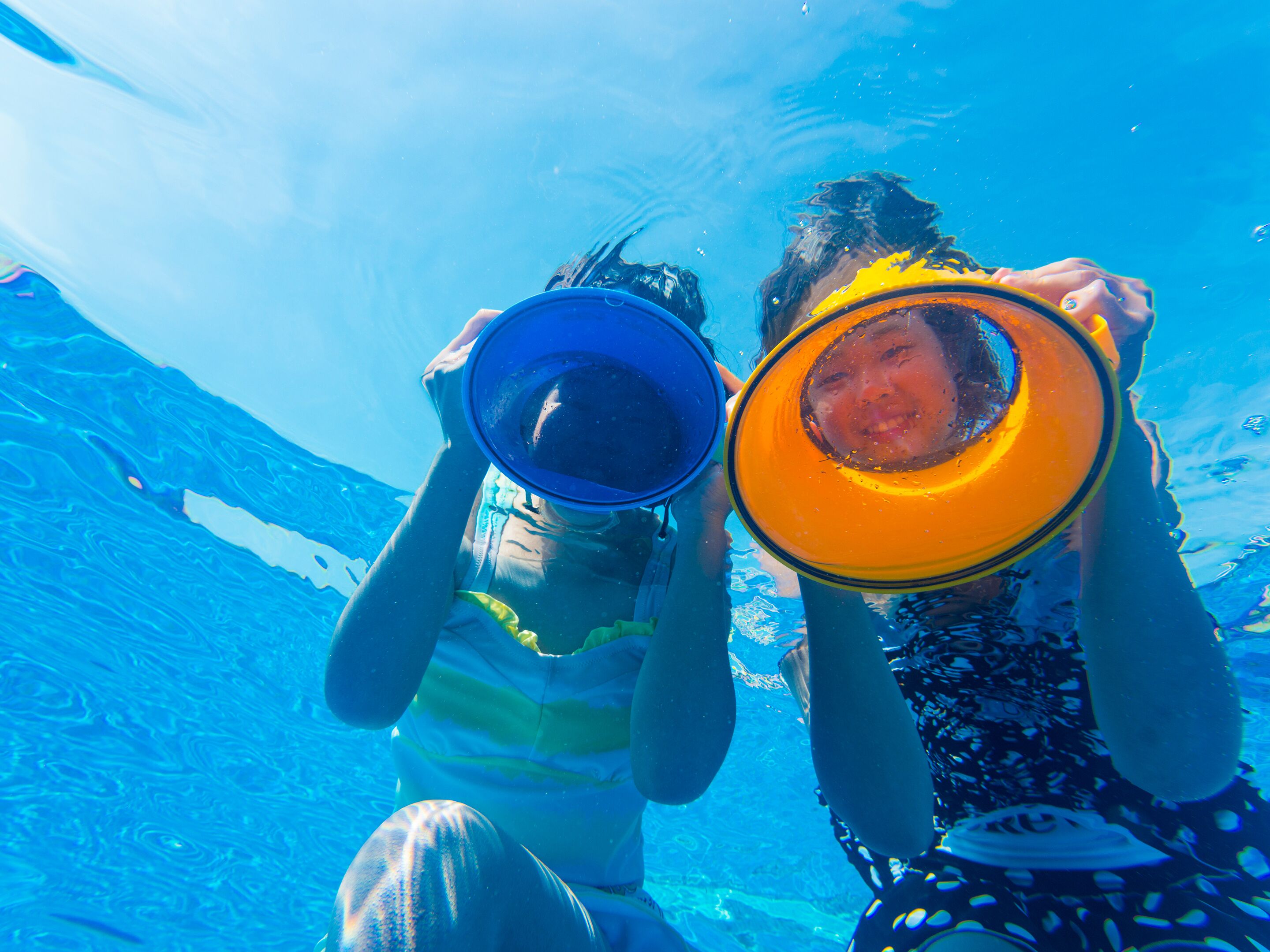 Two people underwater holding a blue and an orange object.
