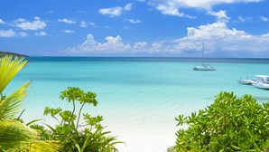 Una playa con agua turquesa cristalina, un velero y abundante vegetación.