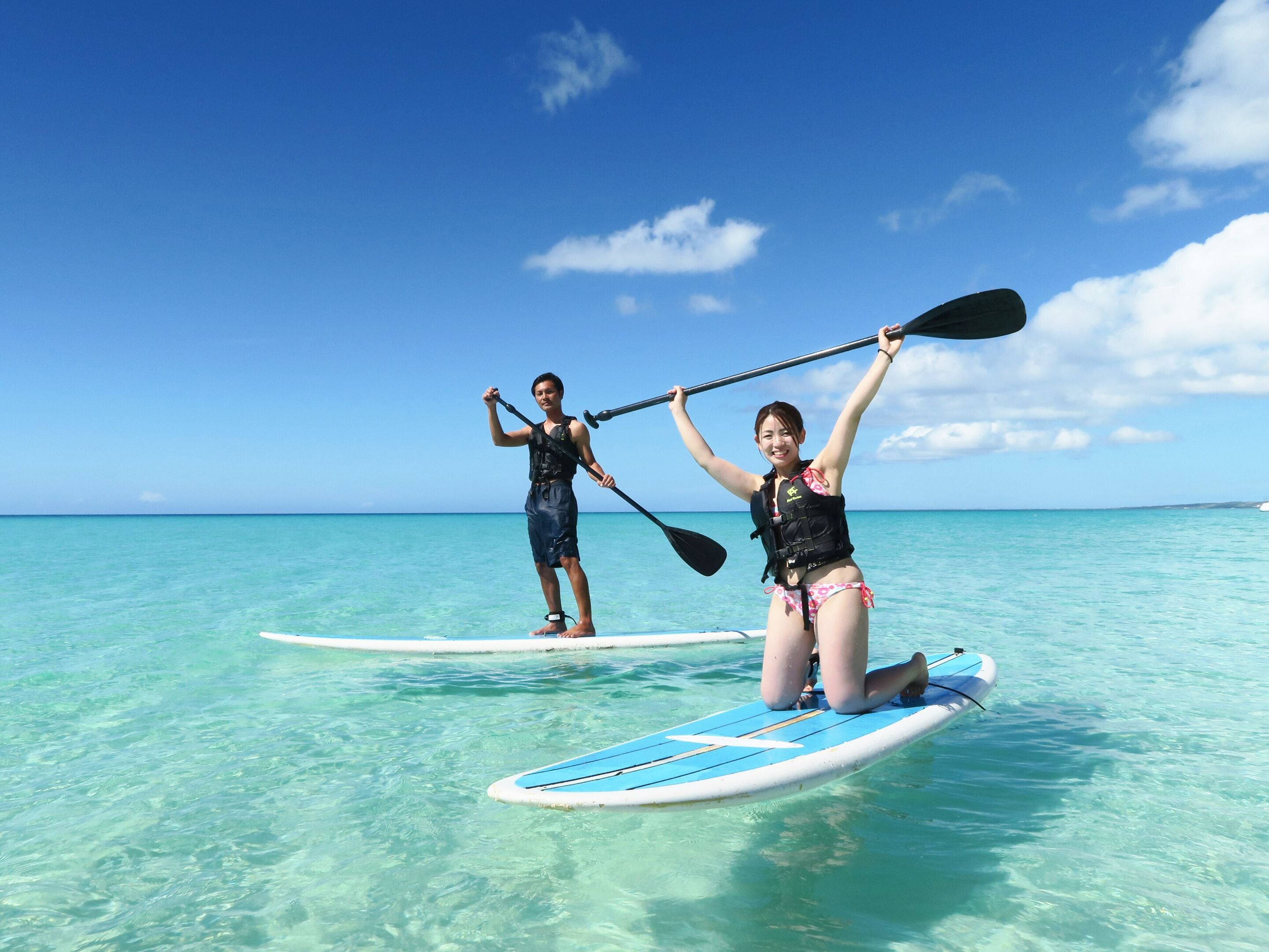 Two people on paddleboards in clear turquoise water with a blue sky.