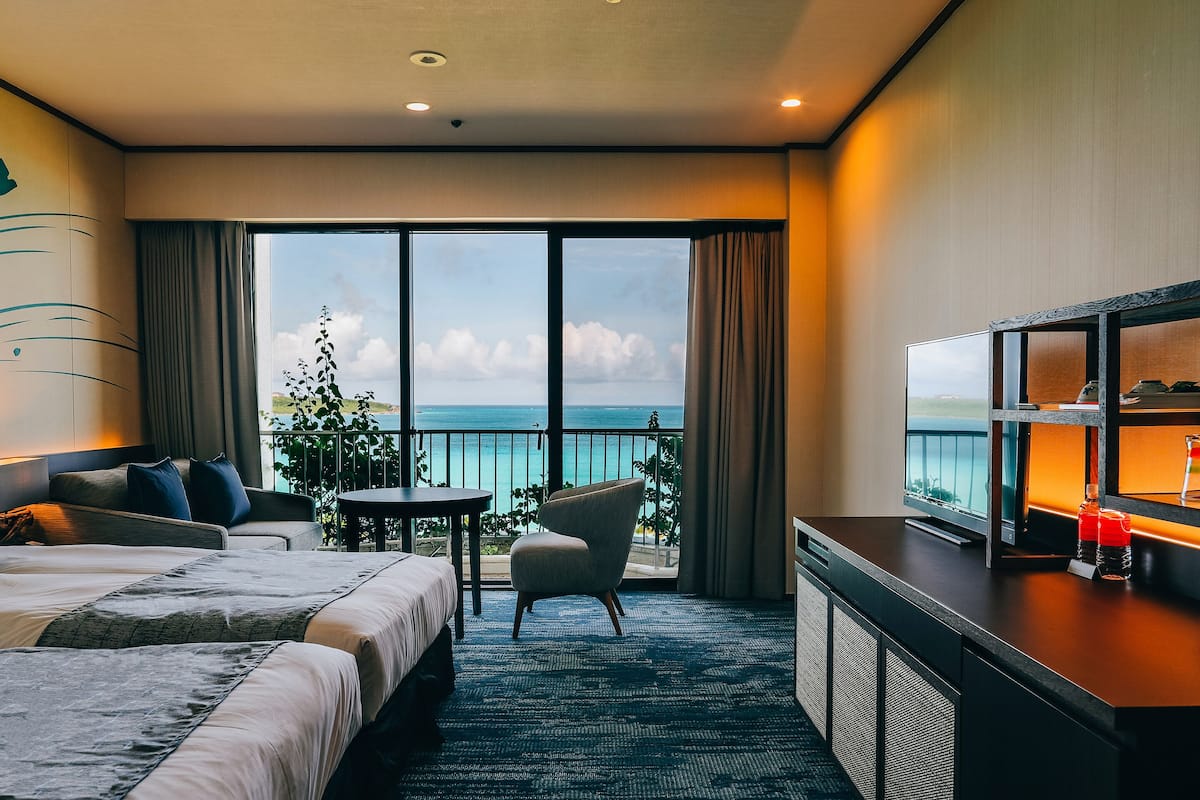 Habitación de hotel con cama, escritorio, silla y vista al océano.