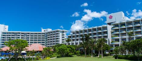 A hotel with multiple floors, balconies with plants, and a clear blue sky.