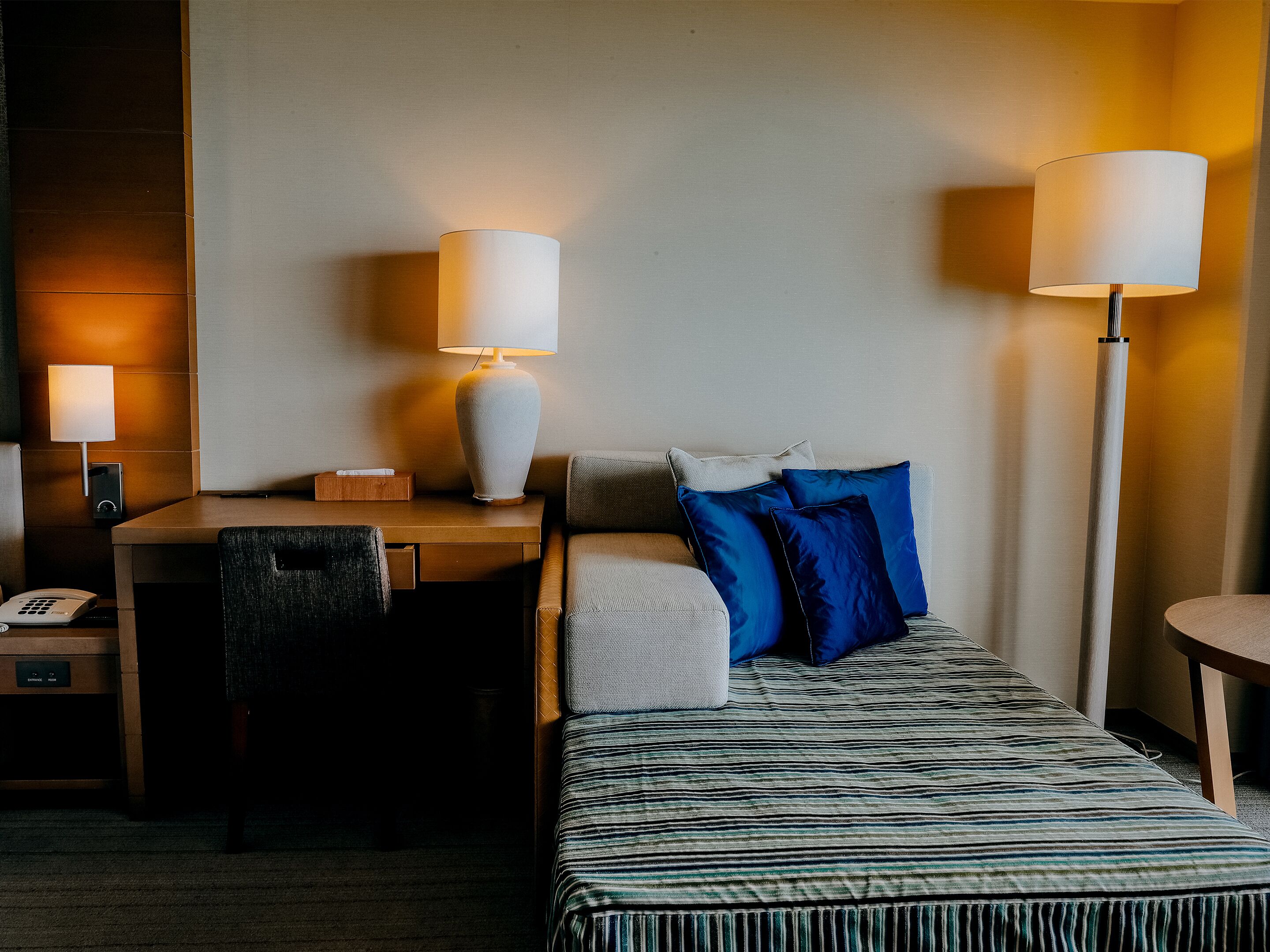 A hotel room with a bed, a desk, a chair, two lamps, and a telephone.