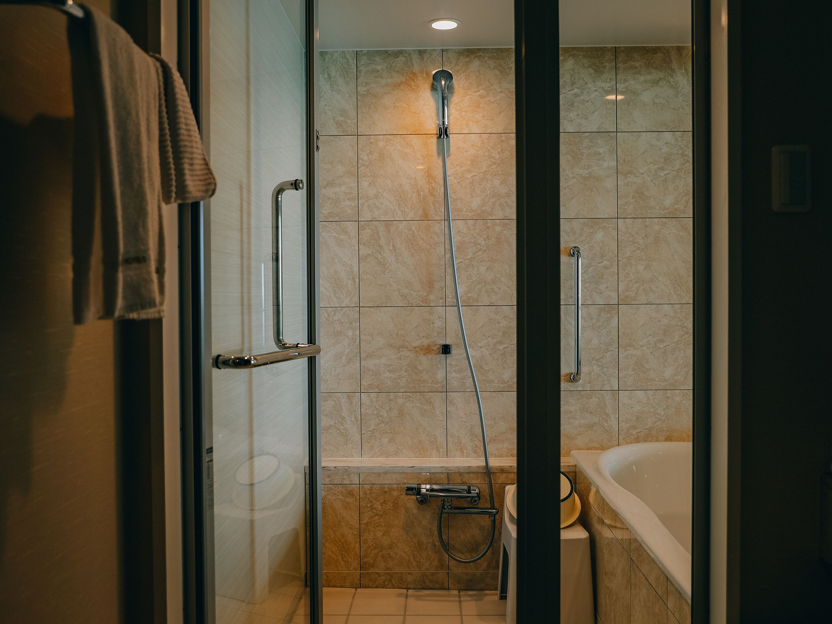 A modern bathroom with a glass shower enclosure, a handheld showerhead, a handheld shower attachment, a grab bar, and a bathtub.