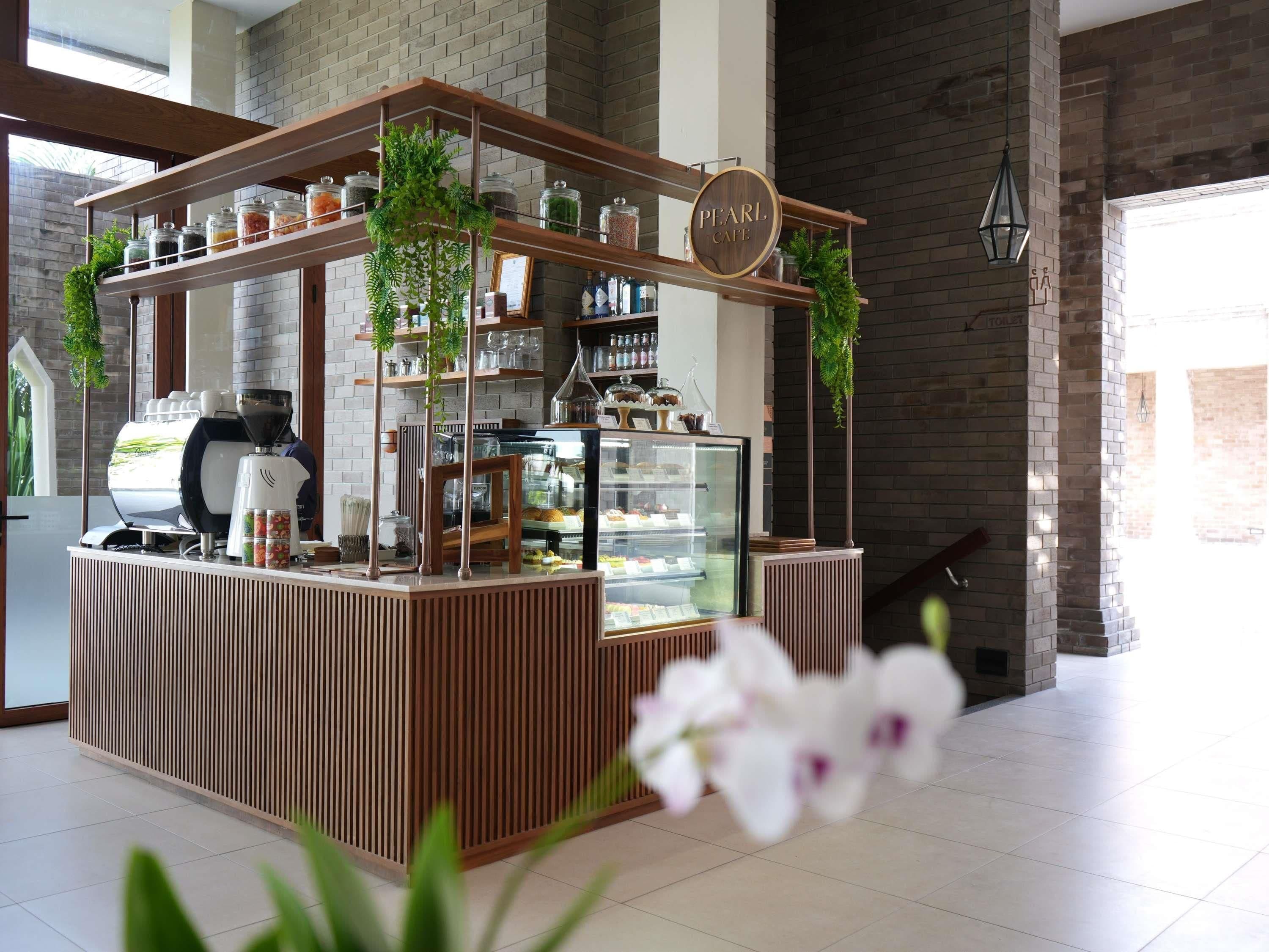 A coffee station with a wooden counter, a glass display case, and shelves with jars and plants.