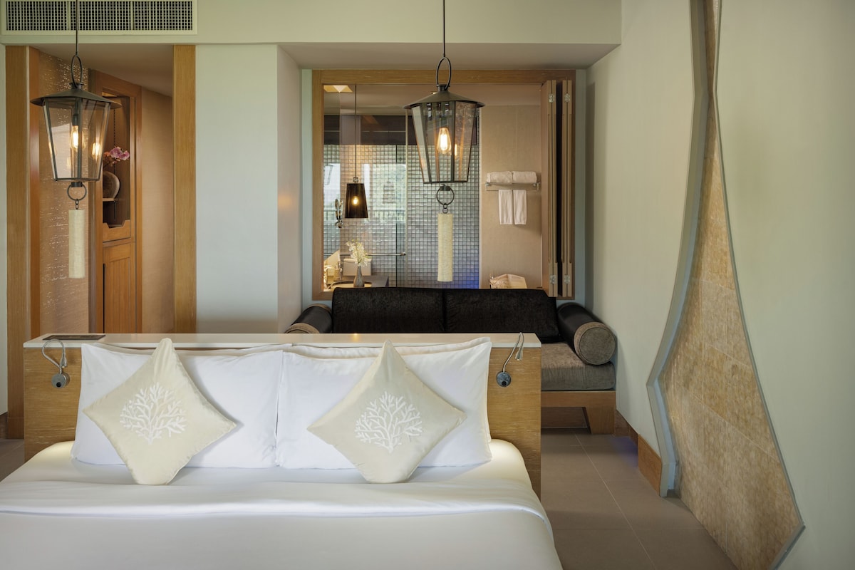 Una habitación de hotel con una cama, dos faroles colgantes, un banco de madera y una pared de azulejos.