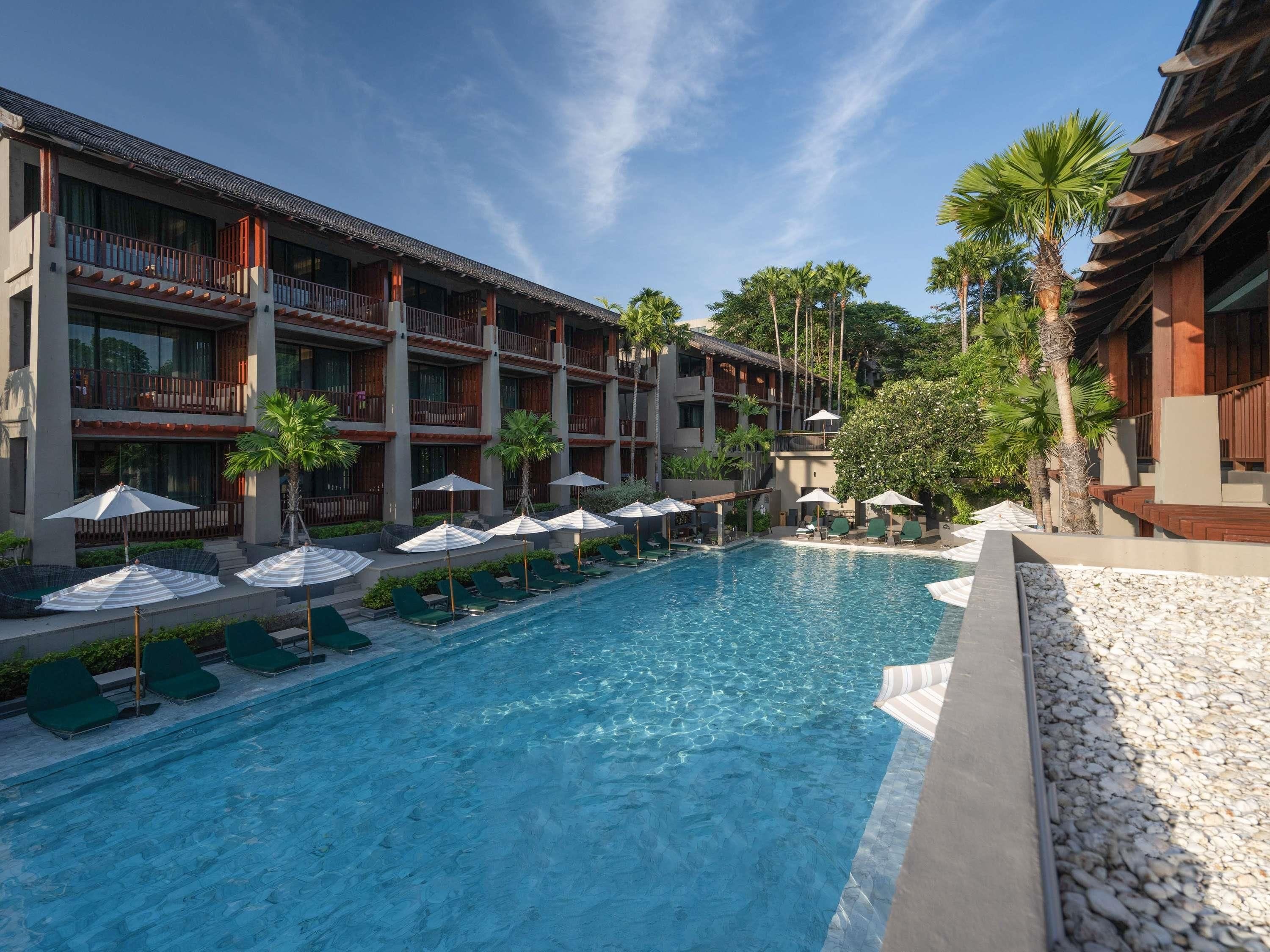 A hotel with a swimming pool, multiple balconies, and palm trees.
