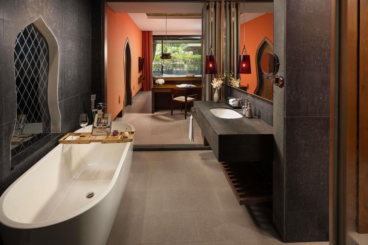 Un baño moderno con una bañera independiente, un tocador con encimera oscura y un espejo grande.