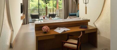 Une chambre d’hôtel avec un bureau en bois, une chaise, une grande fenêtre avec des rideaux, un balcon et une lampe suspendue.