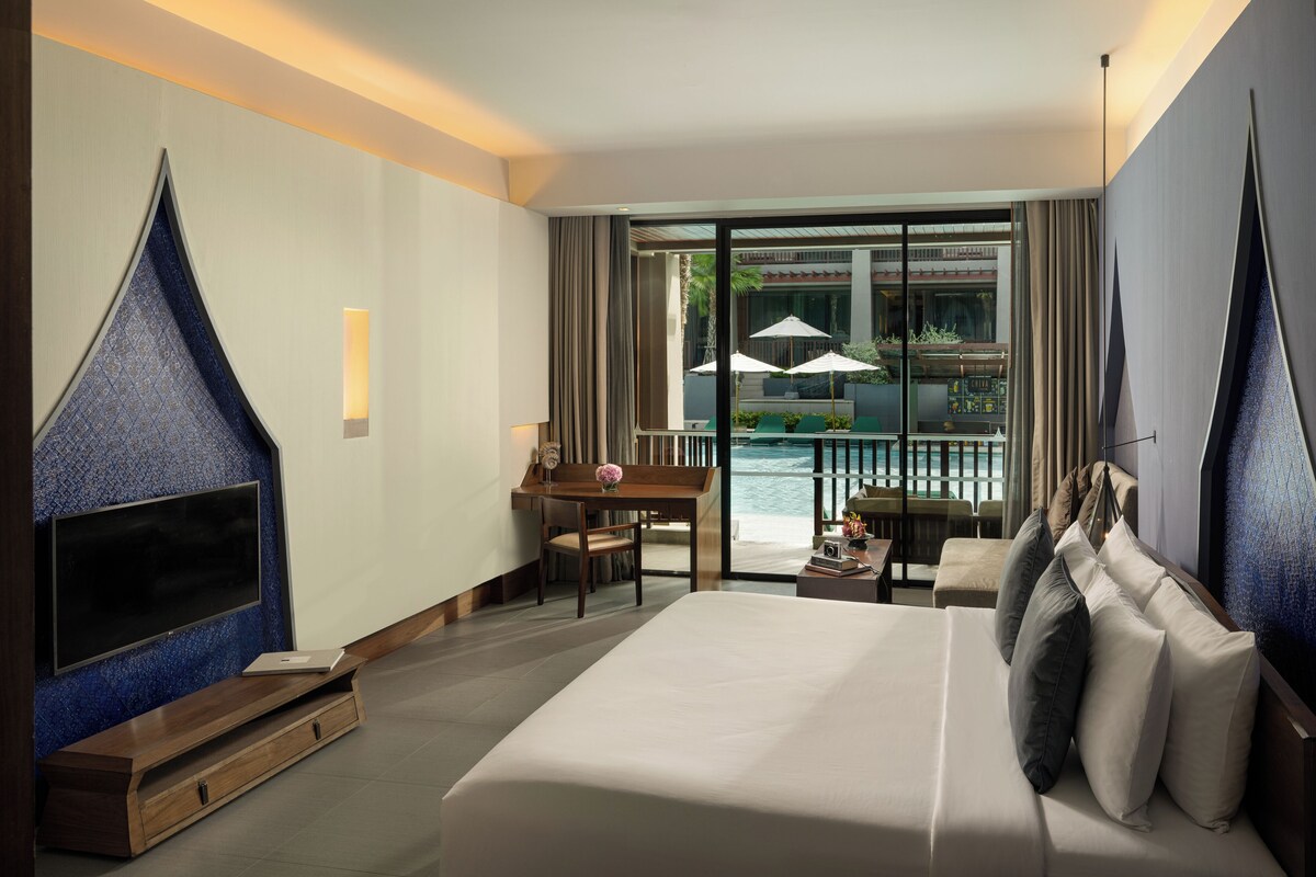 Una habitación de hotel con una cama grande, un escritorio, un televisor y un balcón con vista al mar.