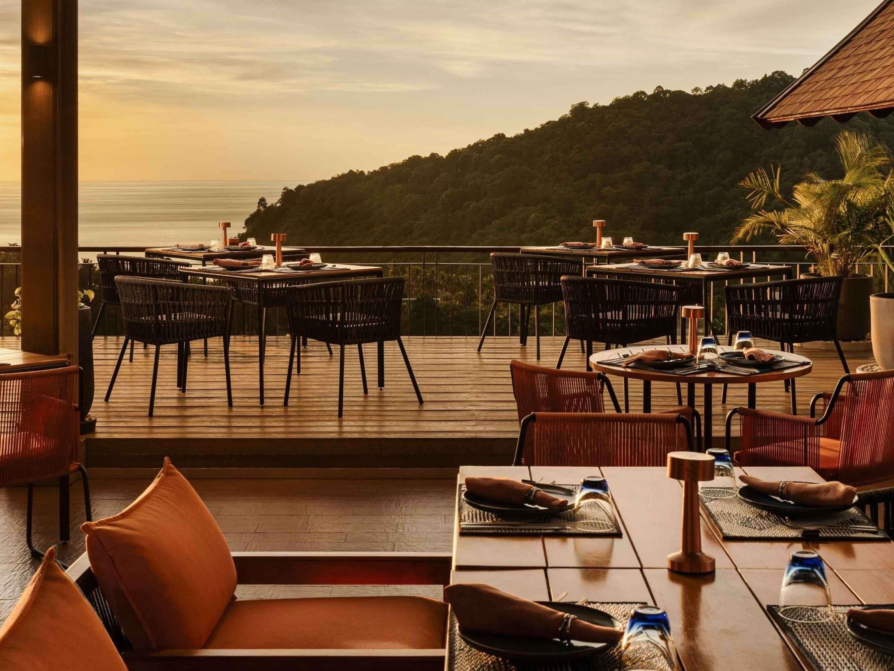 An outdoor dining area with tables and chairs, overlooking a body of water and hills.