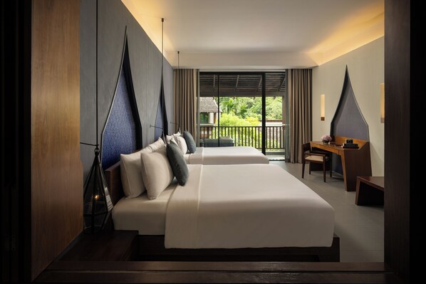 A hotel room with a large bed, a desk, and a view of greenery outside.