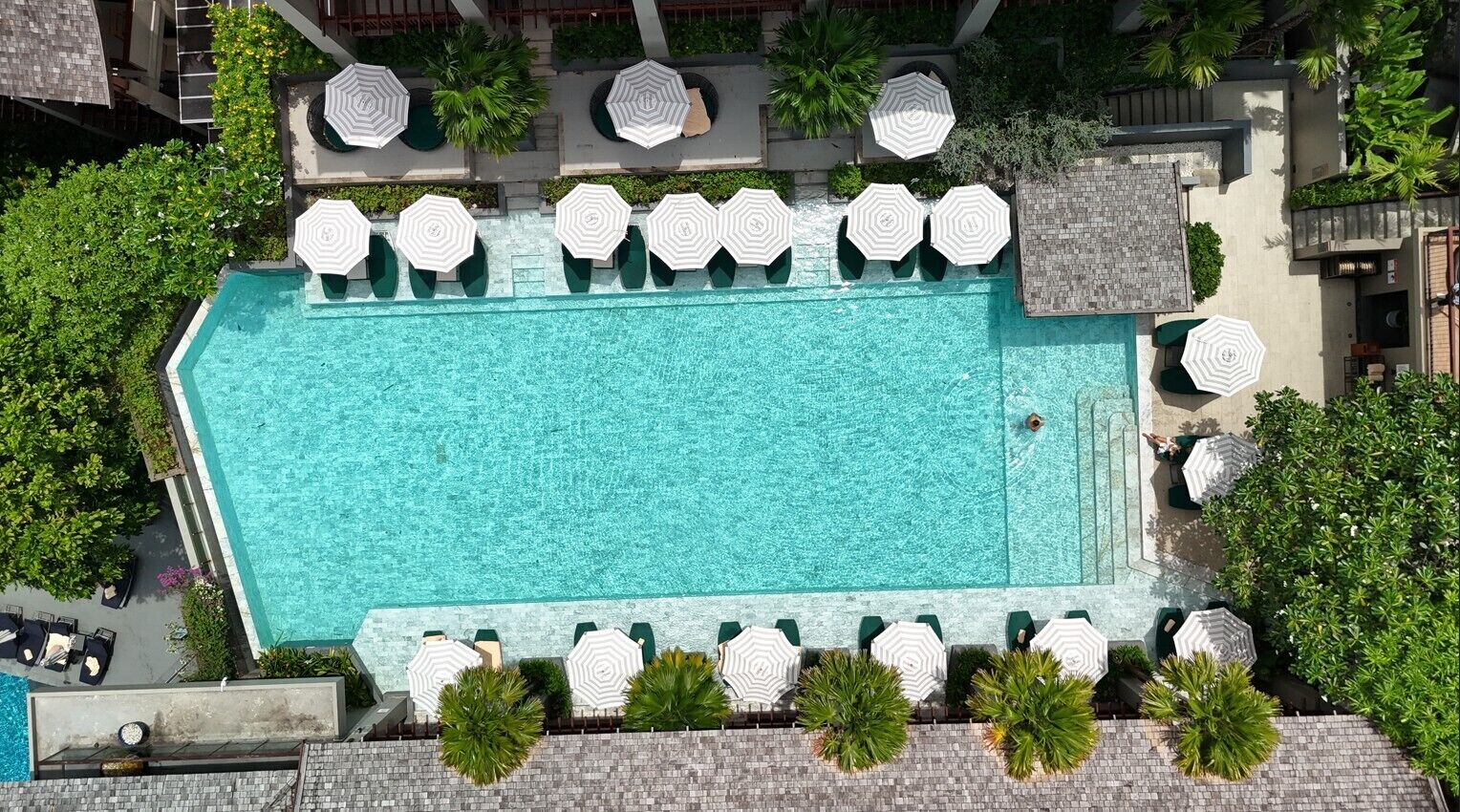An aerial view of a rectangular swimming pool with multiple lounge chairs and umbrellas arranged around it.