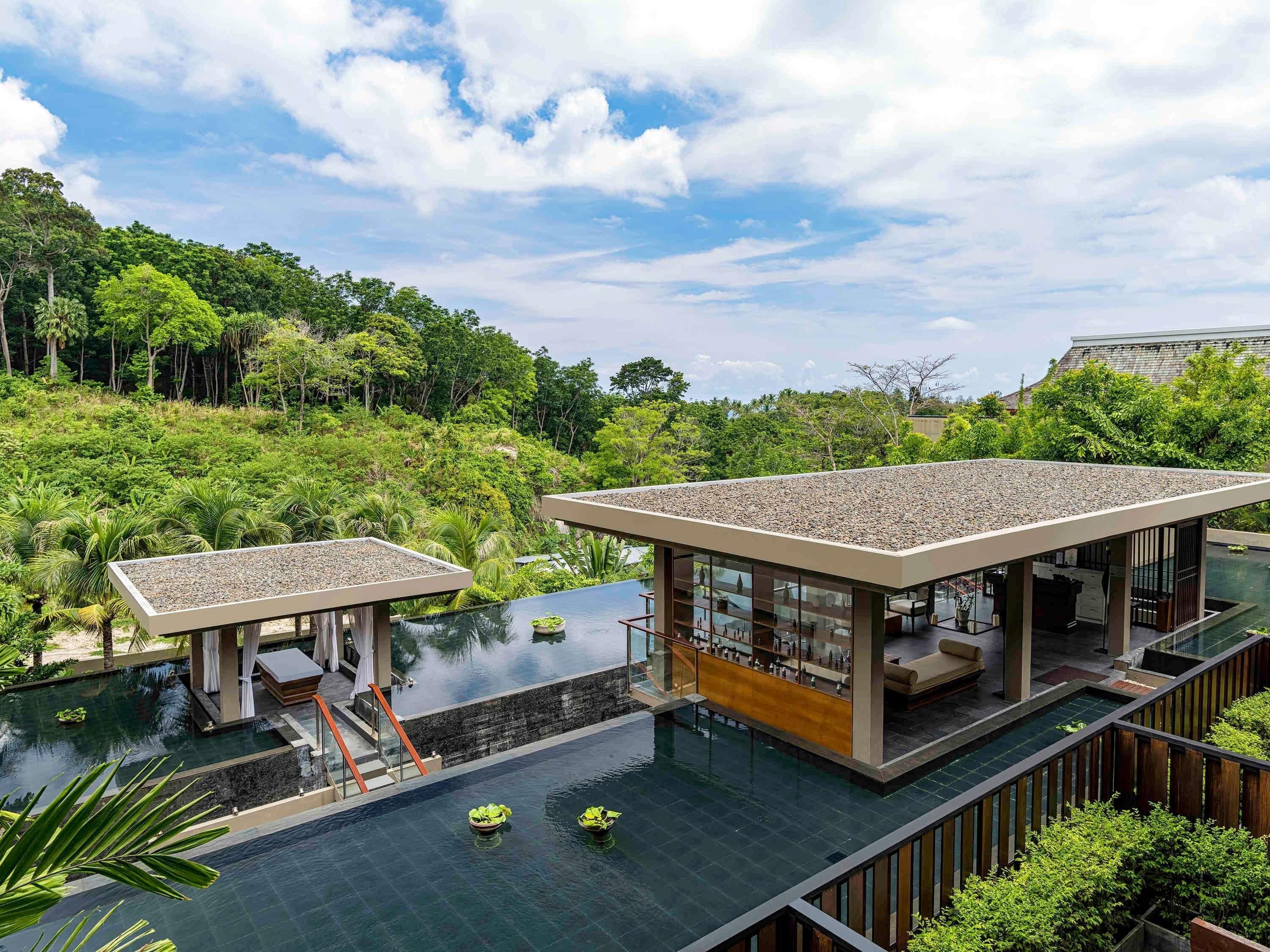 Una villa moderna con piscina, rodeada de exuberante vegetación y un cielo despejado.