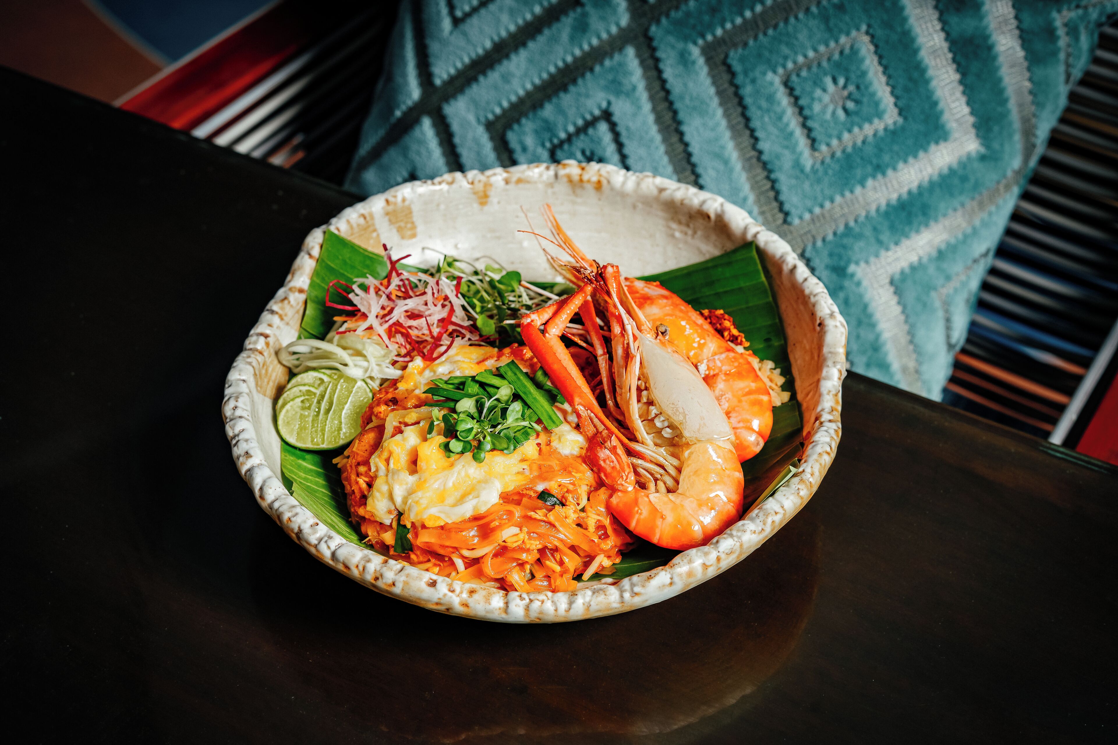 A bowl of food with shrimp, vegetables, and a lime wedge on a table.