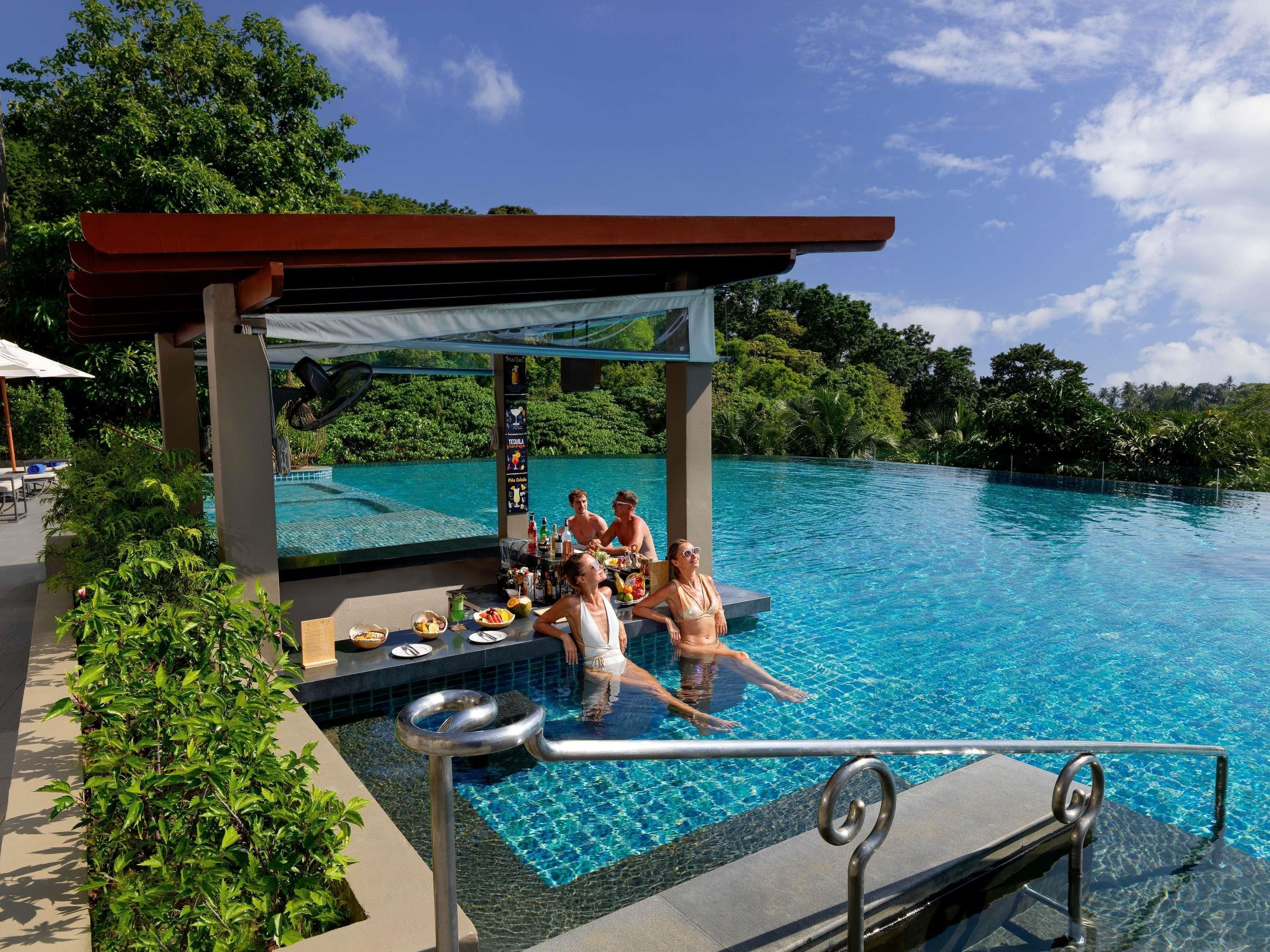 Zona de piscina con bar y sillones de descanso, rodeada de abundante vegetación.