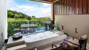 Un baño moderno con una bañera grande, una ducha con cerramiento de vidrio y vistas a vegetación exuberante.