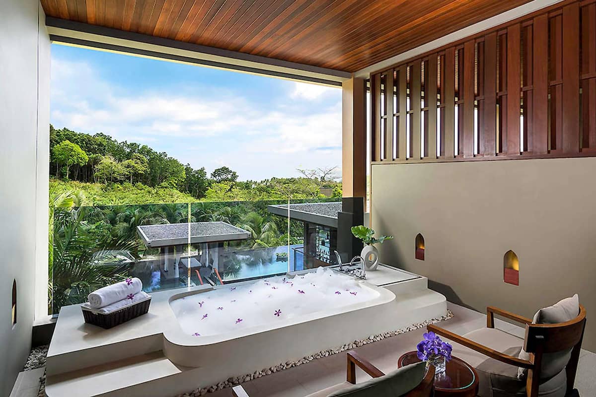 A modern bathroom with a large bathtub, a glass-enclosed shower, and a view of lush greenery.