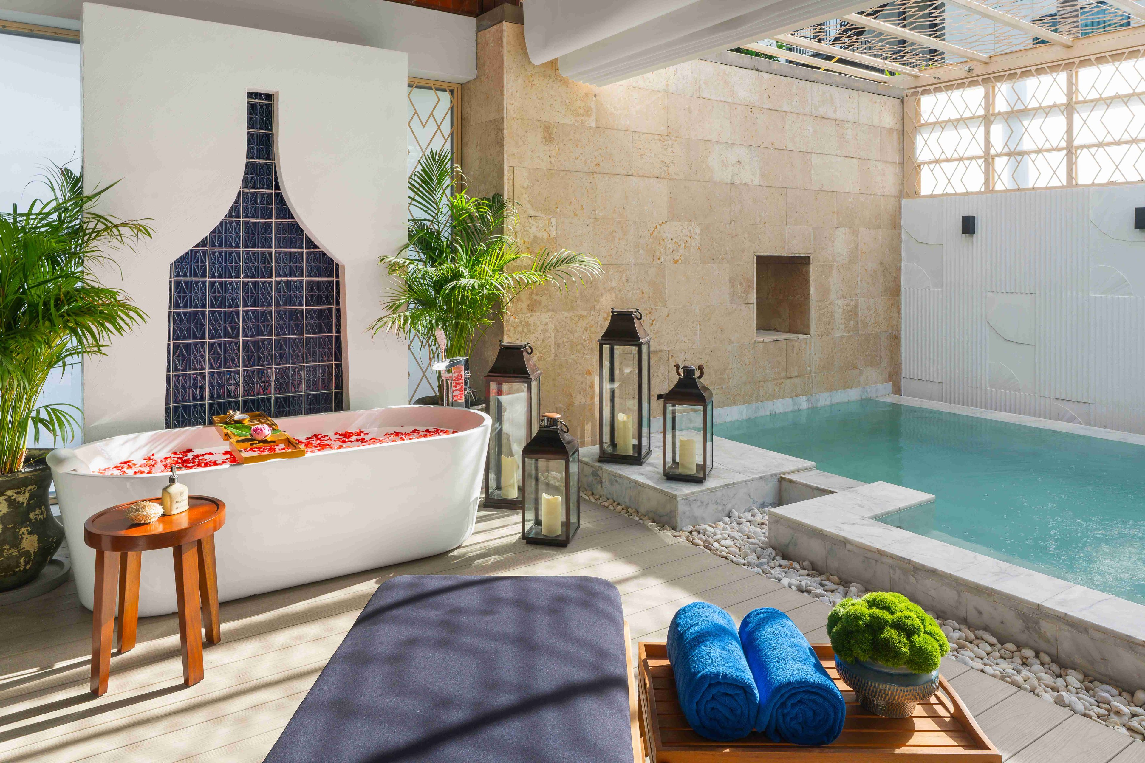 A spa area with a large bathtub, a lounge chair, a small table with towels, and a pool.