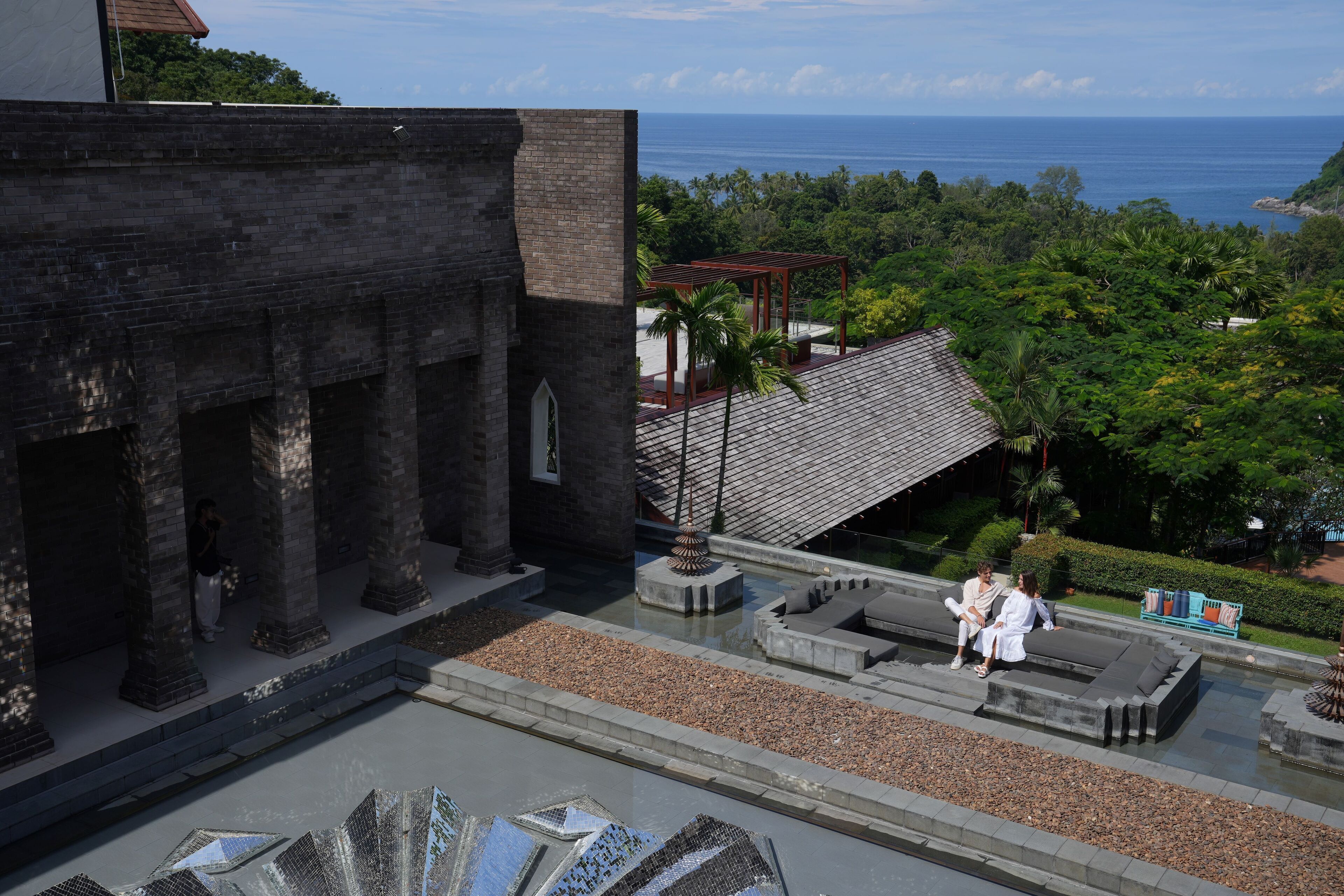 Un patio con un edificio de ladrillo, una fuente de agua y vista al océano.