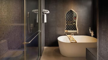 Un baño moderno con una bañera independiente, ducha con cerramiento de vidrio y pared con azulejos oscuros.