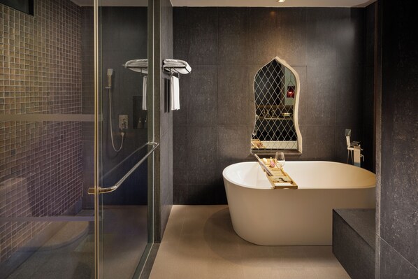 Un baño moderno con una bañera independiente, ducha con cerramiento de vidrio y pared con azulejos oscuros.