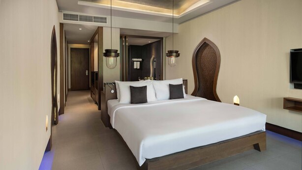 A hotel room with a large bed, a TV, and a bathroom visible through an open door.