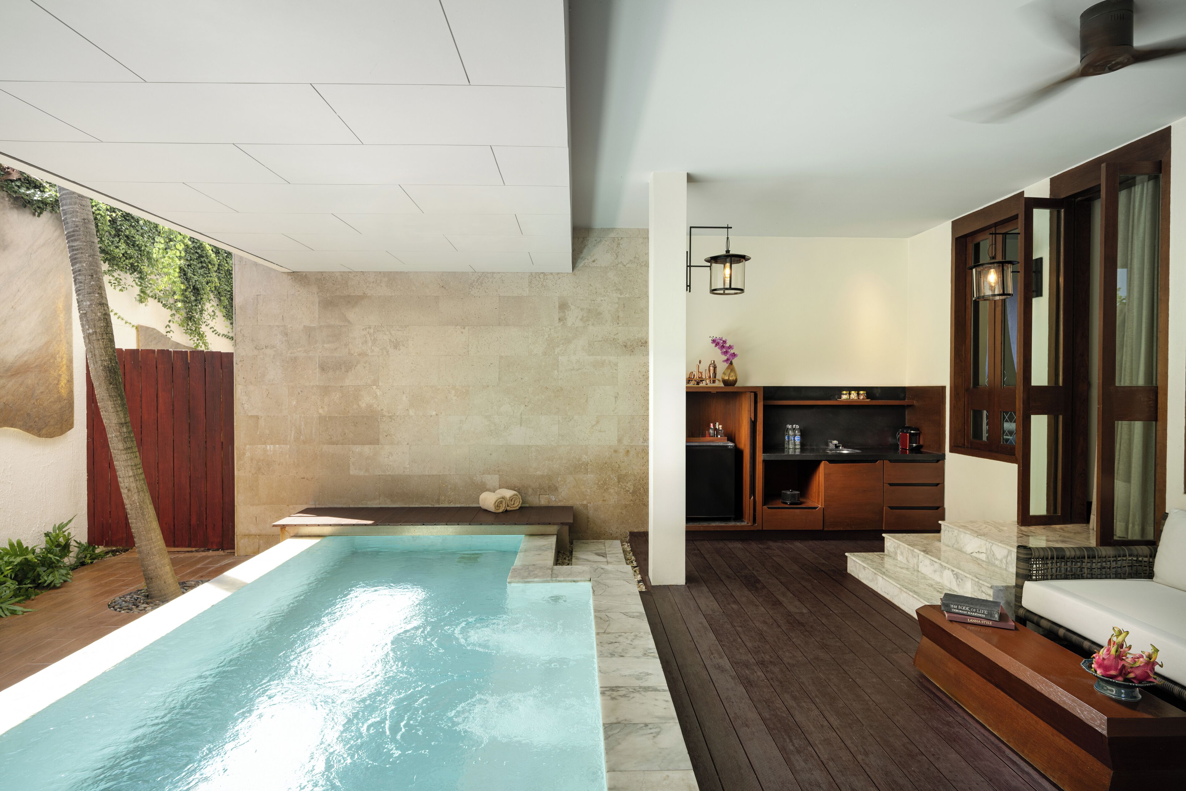 A modern outdoor pool area with a wooden deck, a built-in seating area, and a small kitchen space with a dining table and chairs.