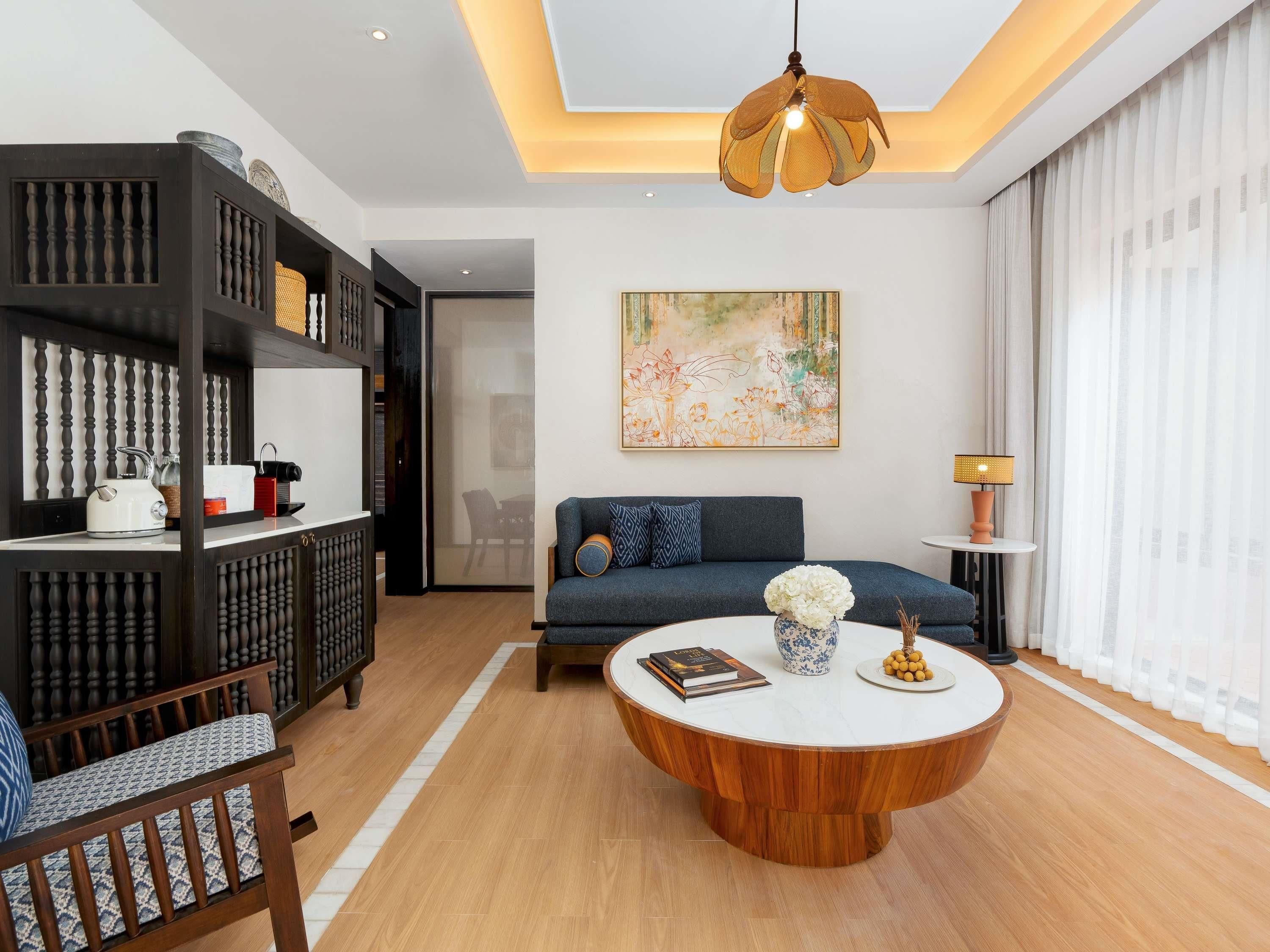 A modern living room with a round wooden coffee table, a sofa, a bookshelf, and a large abstract painting on the wall.