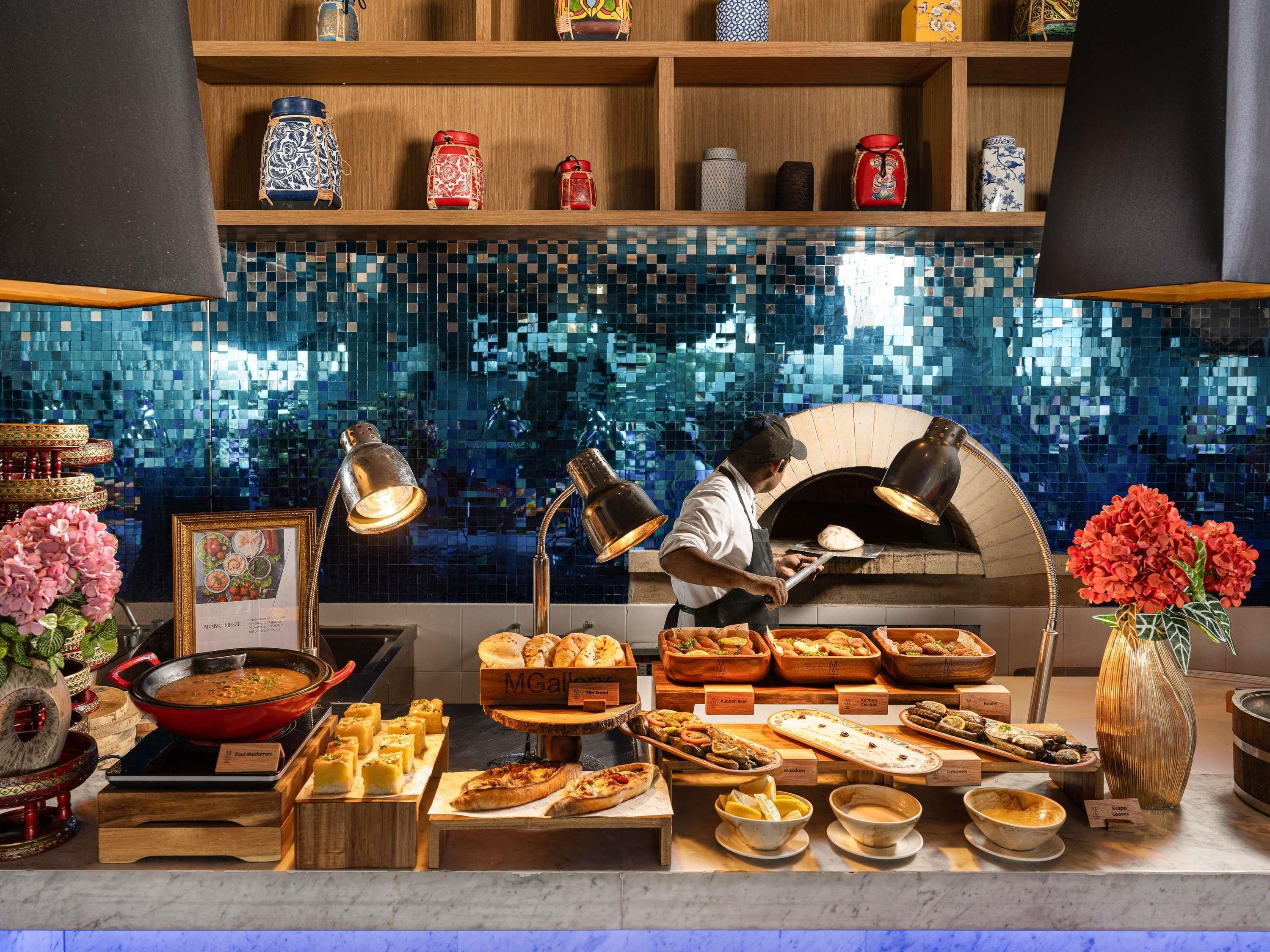 A food display area with various baked goods and a person cooking in a brick oven.