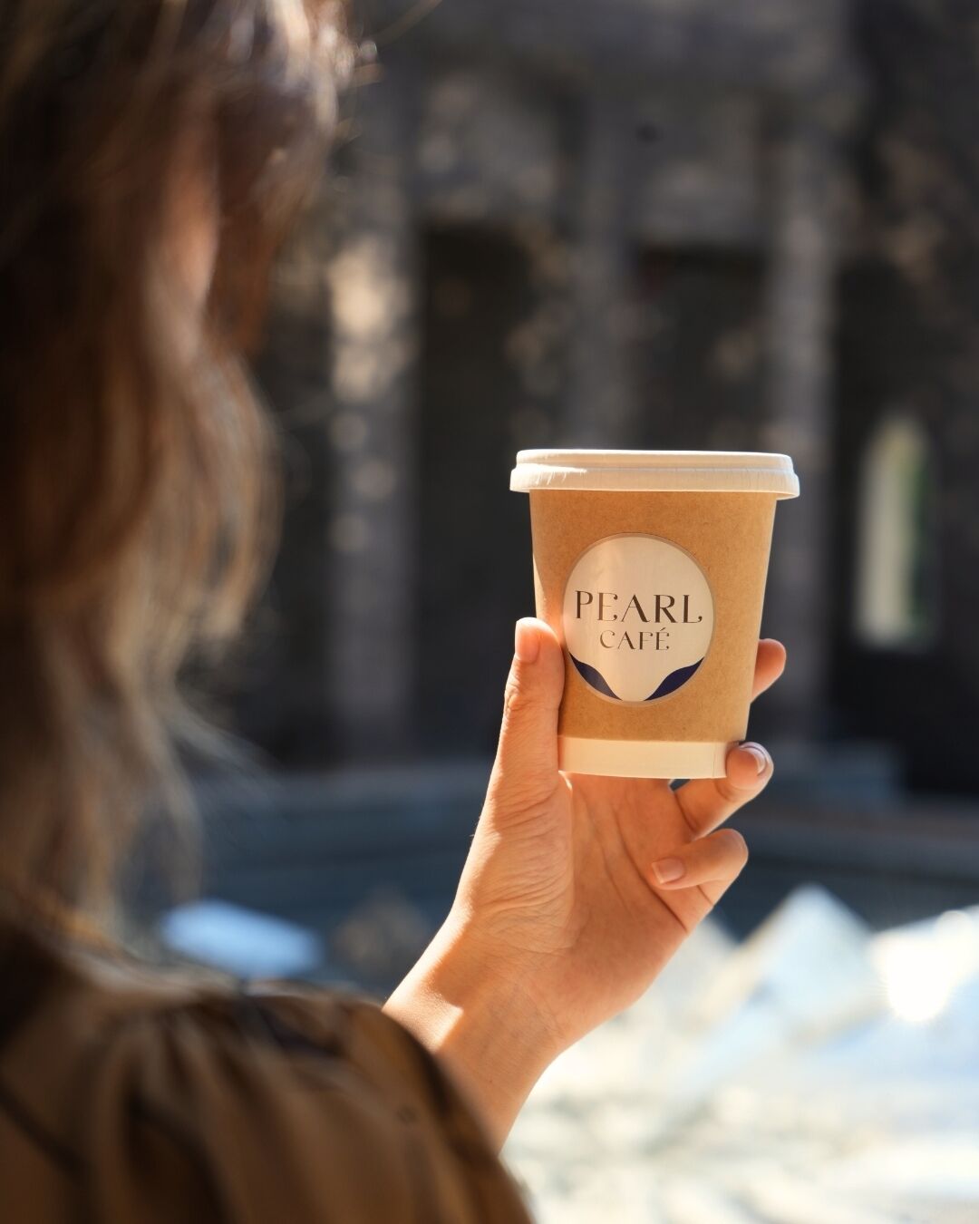 A person holding a coffee cup with "PEARL Café" written on it.