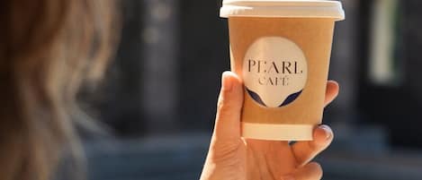 A person holding a coffee cup with "PEARL CafĂŠ" written on it.