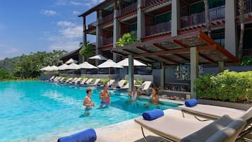 A pool area with lounge chairs and umbrellas, a bar, and a building with multiple balconies.