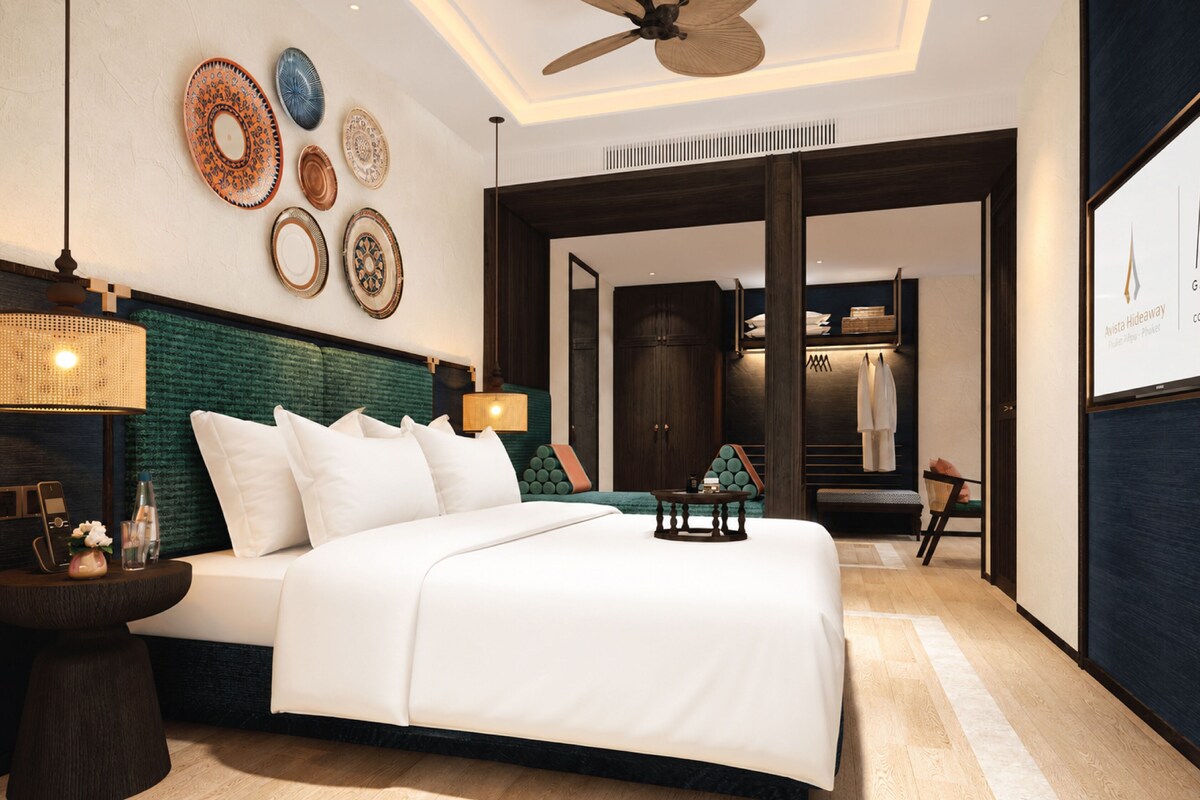 A modern hotel room with a large bed, a ceiling fan, decorative plates on the wall, and a view of the hallway.
