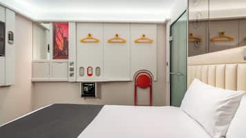 Habitació d'hotel amb llit, armari amb penjalls, mirall i una cadira vermella.