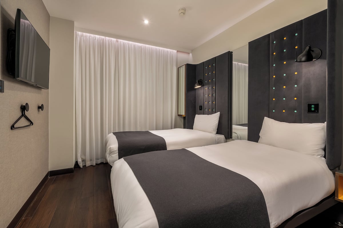 A hotel room with two beds, a TV, a mirror, and a window with curtains.