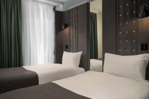 A hotel room with two beds, a large mirror, a wall-mounted lamp, and a window with curtains.