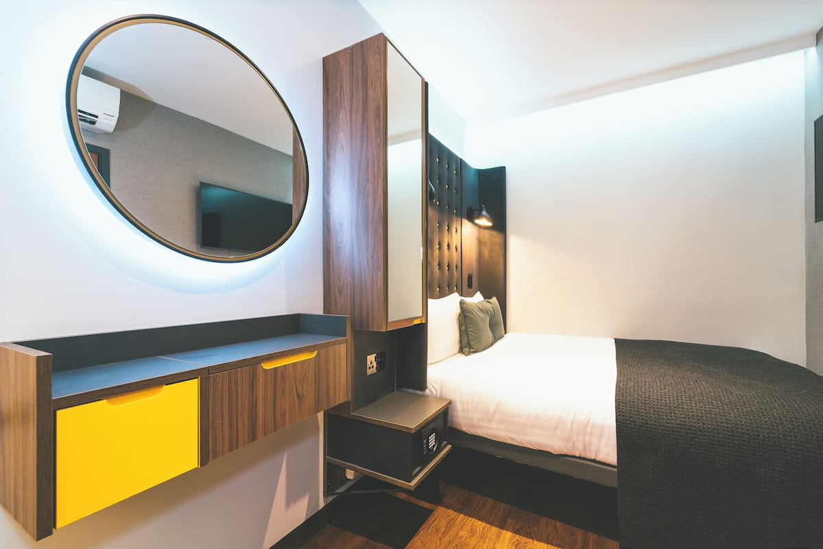 A modern hotel room with a bed, a bedside table, a mirror, and a wardrobe.