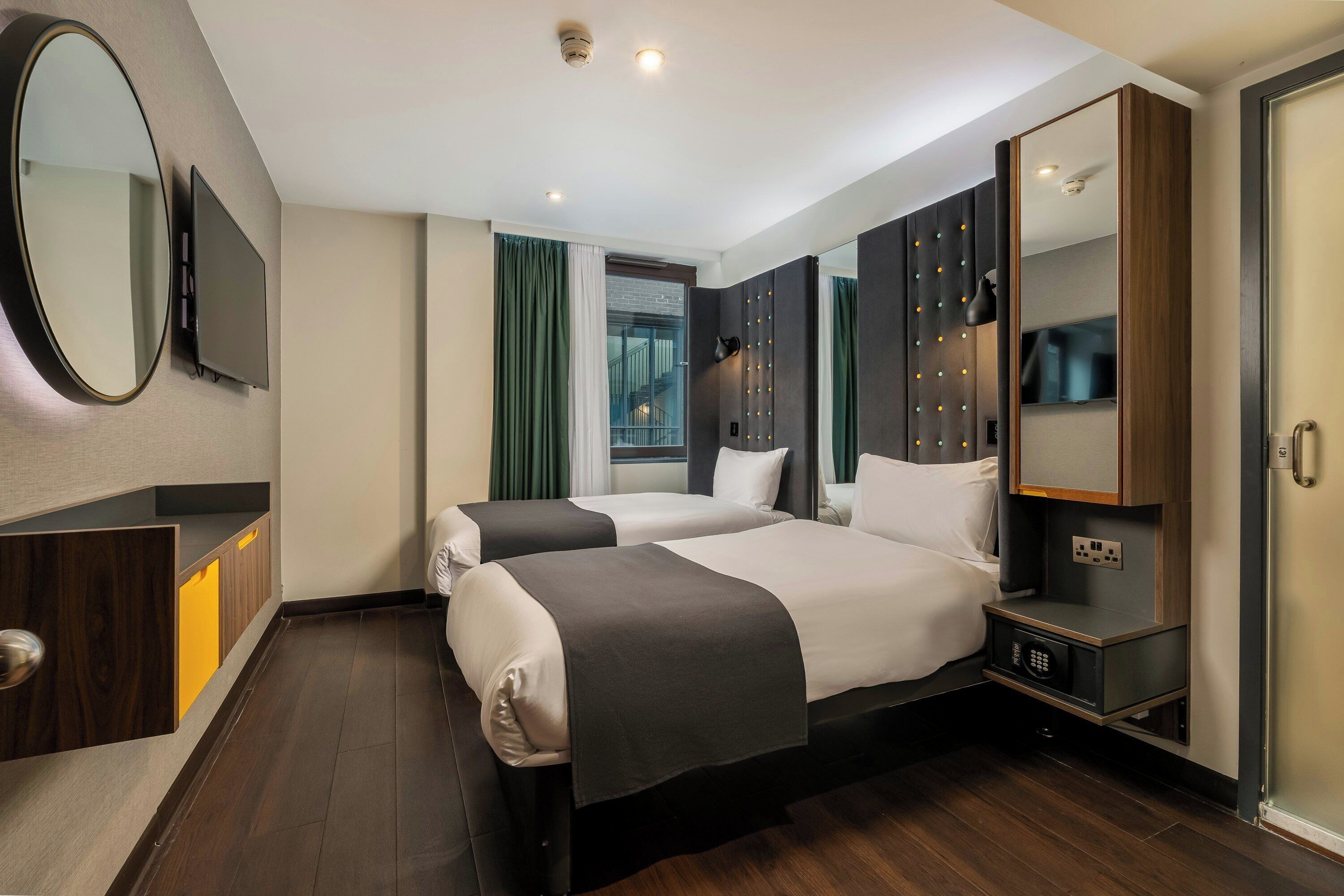 Een hotelkamer met twee bedden, een grote spiegel, een televisie en een kledingkast.
