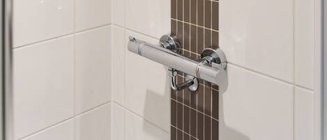 A shower with a handheld showerhead, a control panel, and a towel bar.