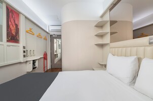 Camera d'albergo moderna con un letto grande, un armadio pieno di vestiti, uno specchio e vista sulla città.