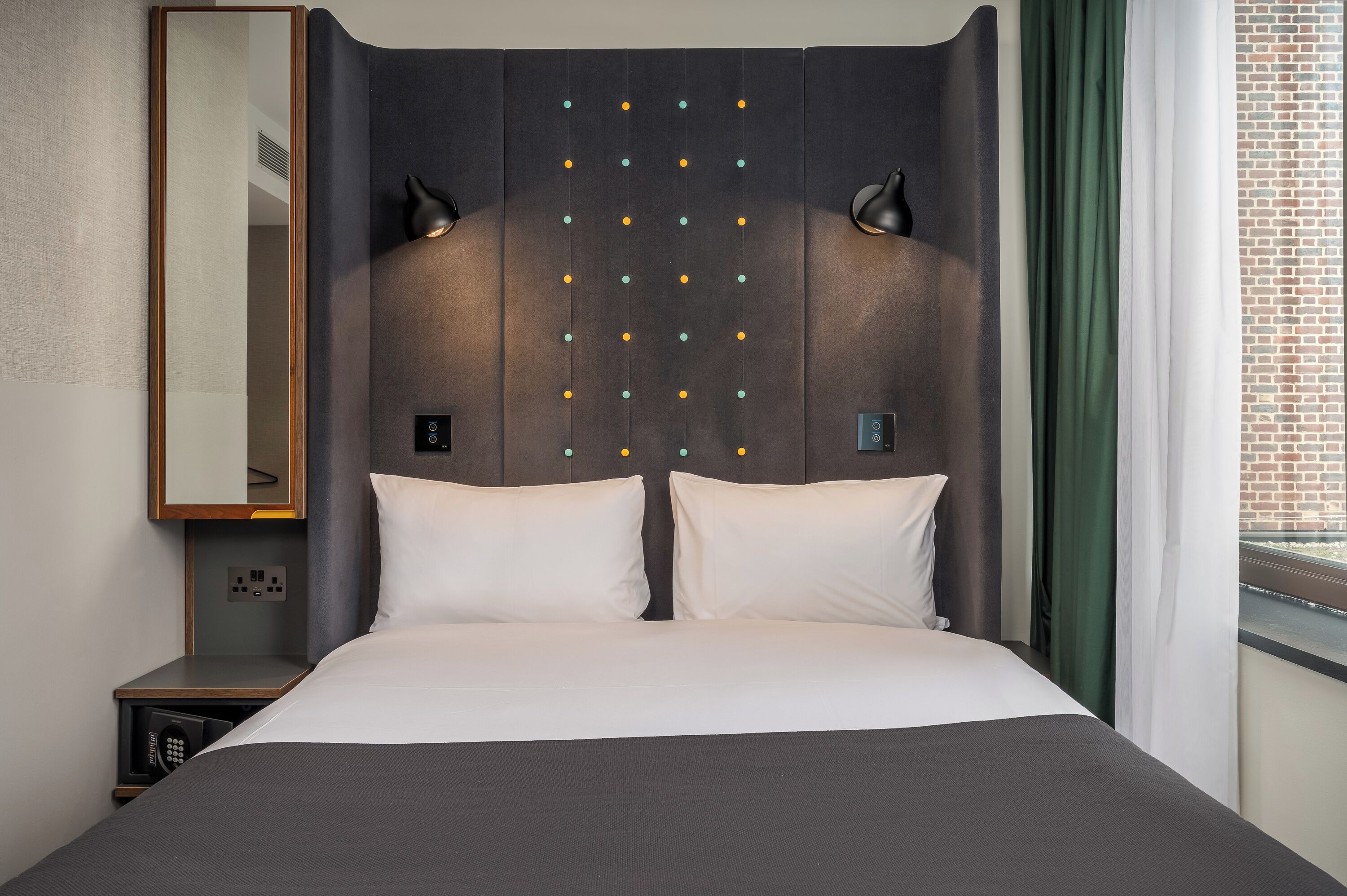 A hotel room with a large bed, bedside lamps, a nightstand, a mirror, and a window with curtains.