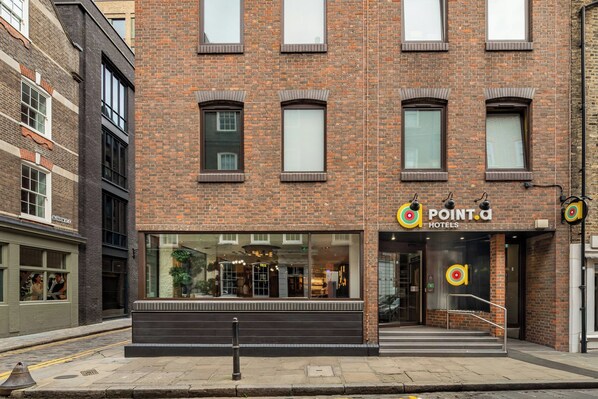 A hotel with a brick facade, large windows, and a visible entrance with a check-in desk.
