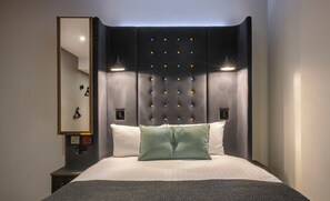 A modern hotel room with a large bed, a headboard with a tufted design, two bedside lamps, and a mirror on the wall.