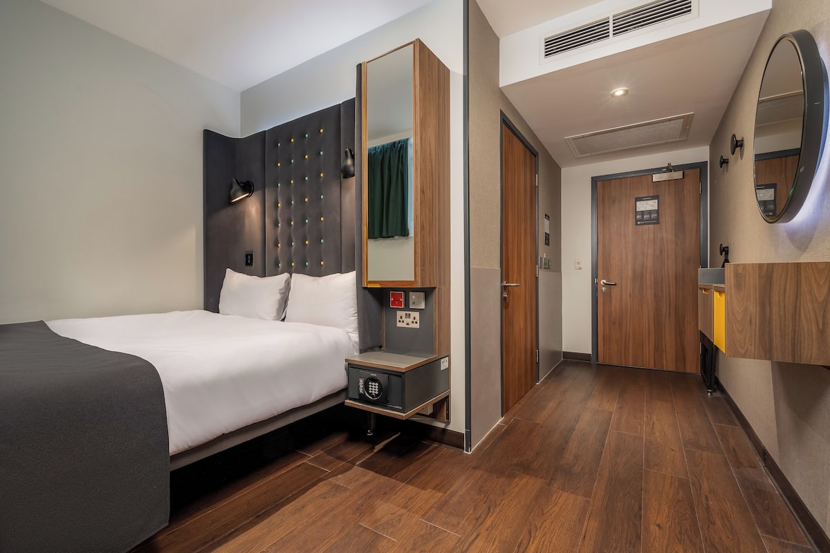A modern hotel room with a bed, bedside table, and a large mirror.
