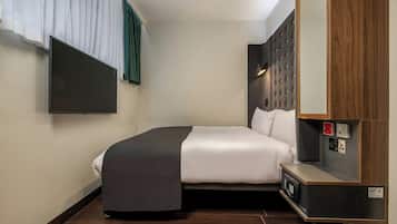 Une chambre d’hôtel comprenant un lit, un téléviseur à écran plat fixé au mur, une table de chevet avec une lampe et un panneau en bois sur le mur.