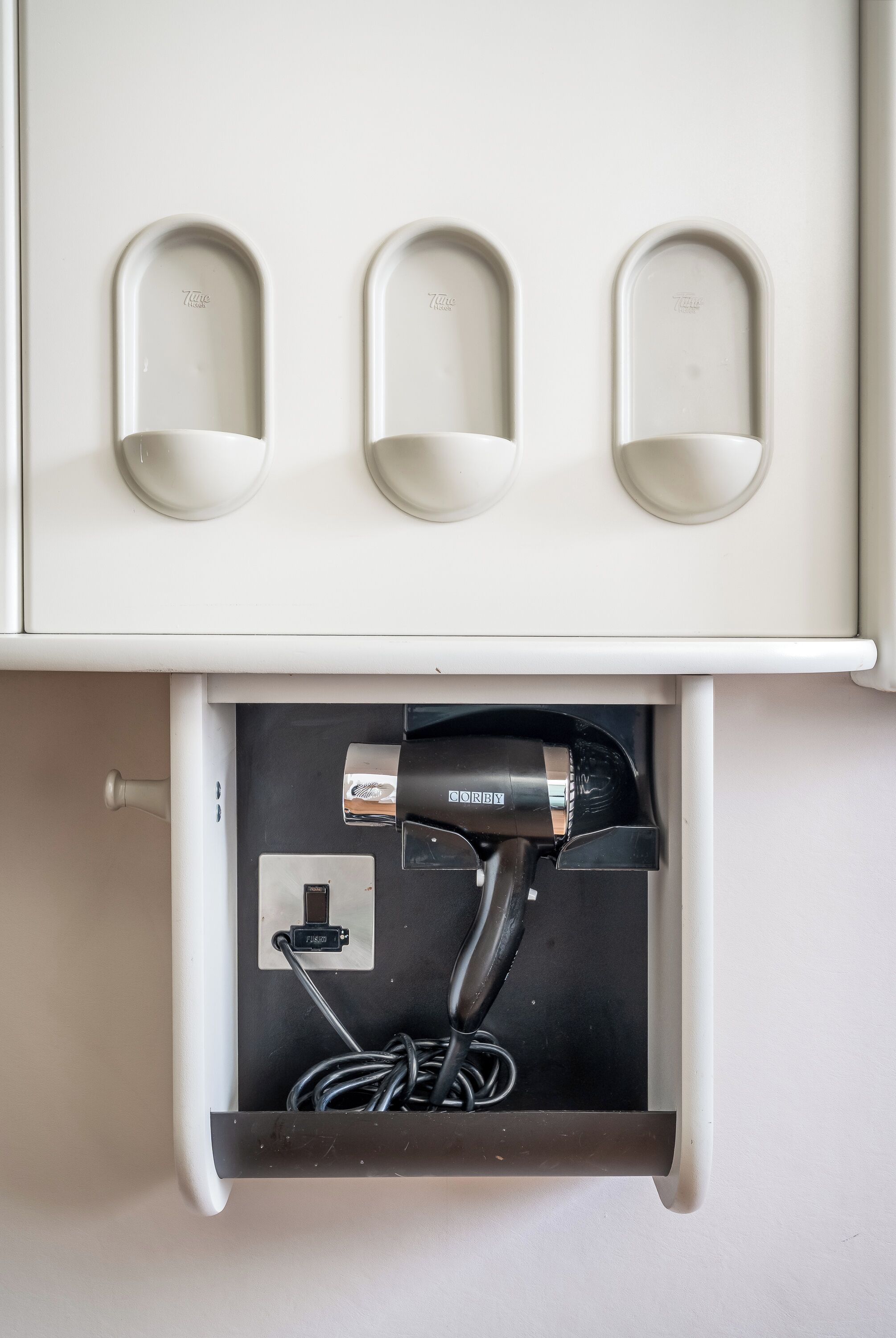 A white cabinet with three cup holders and a hair dryer plugged in below.
