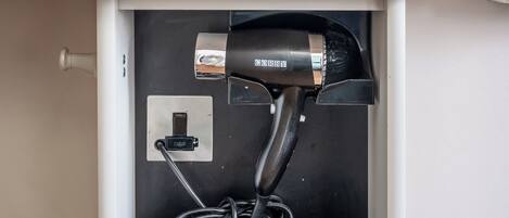 A white cabinet with three cup holders and a hair dryer plugged in below.