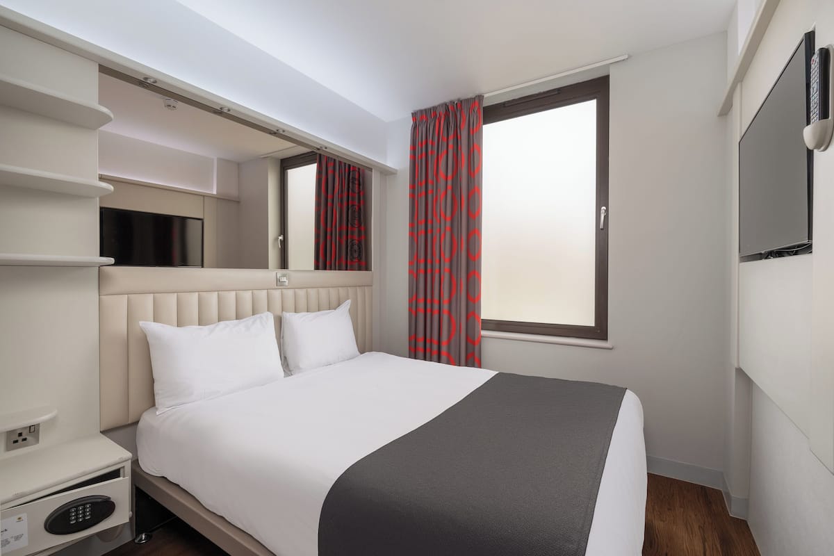A hotel room with a bed, bedside table, and a TV mounted on the wall.