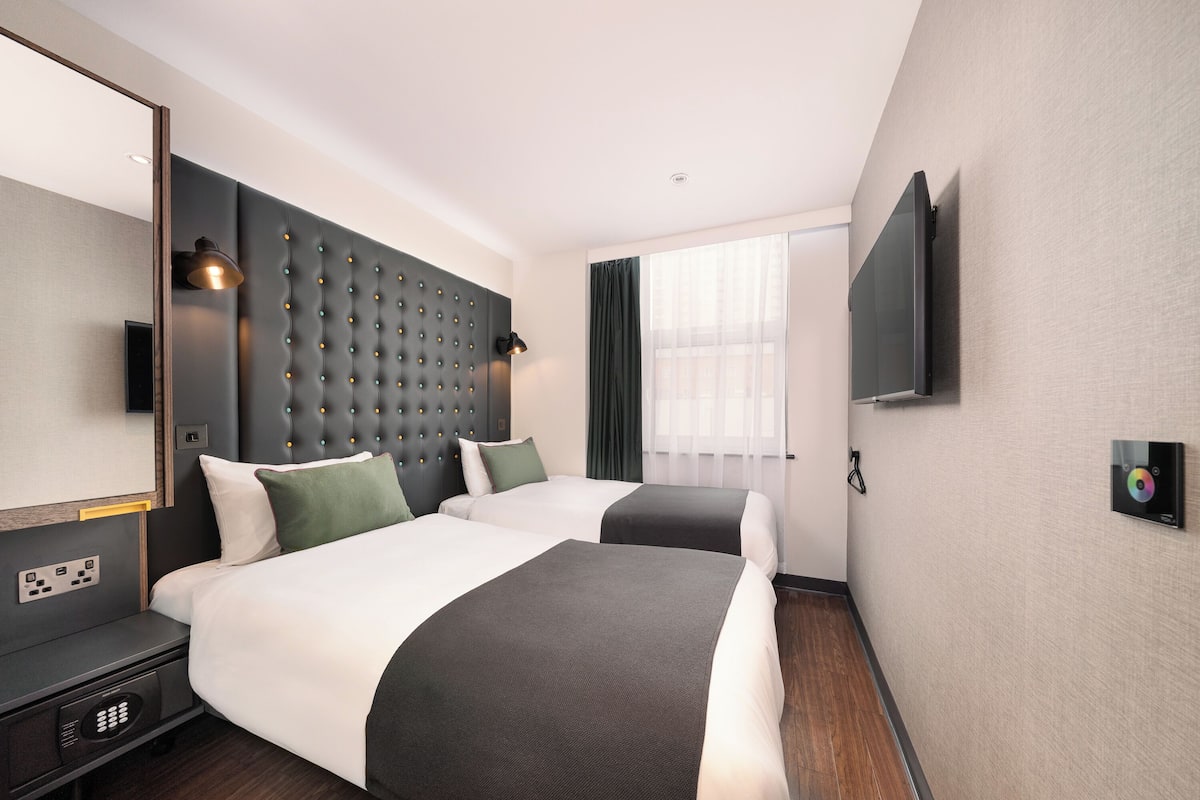 Ein Hotelzimmer mit zwei Betten, einem großen Spiegel, einem Flachbildfernseher und einem Fenster mit Vorhängen.