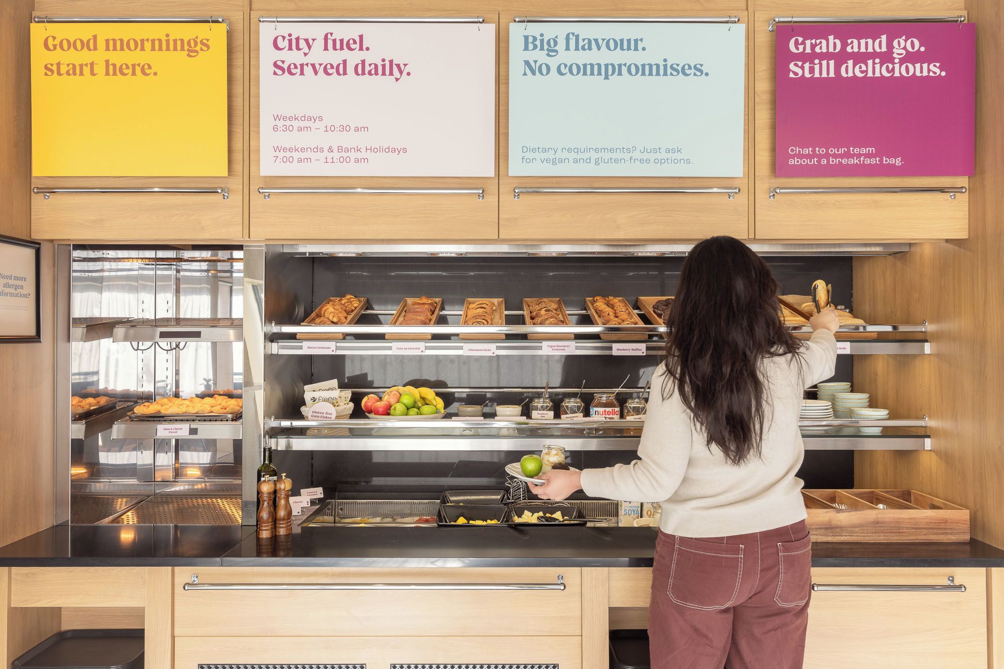 A breakfast counter with various food items and a person serving.